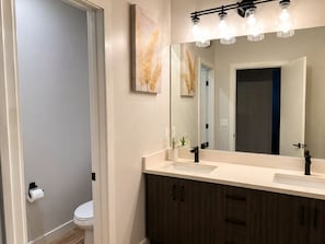 A bathroom with a white sink, dark wooden cabinets, a large mirror, and a toilet.