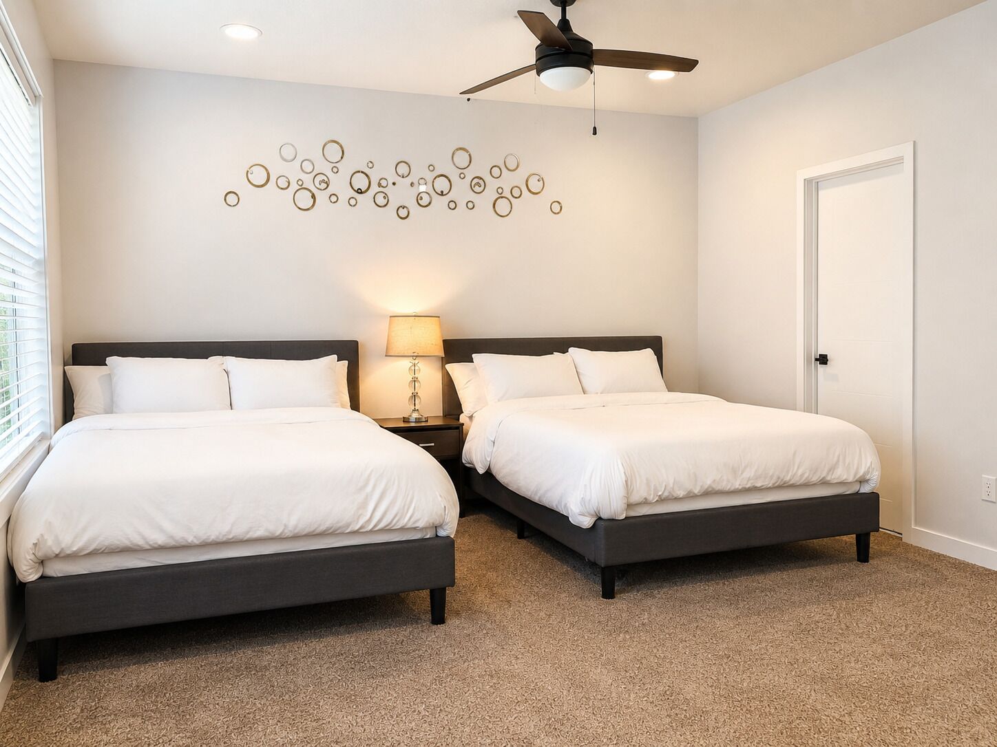 A hotel room with two beds, a ceiling fan, a wall art piece, and a door.