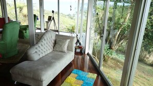 Ein geräumiges Wohnzimmer mit einem großen Fenster, einem grünen Sessel, einem weißen Sofa und einem farbenfrohen Teppich.
