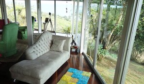 Un salón espacioso con un ventanal grande, un sillón verde, un sofá blanco y una alfombra colorida.