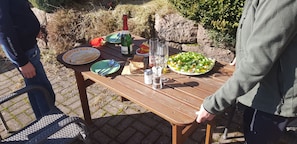 A picnic table set outdoors with plates, cutlery, a bottle of champagne, and glasses.