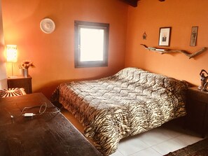 A bedroom with a zebra-patterned bedspread, a small bedside table with a lamp, and a window with a view of the outside. - The health residence (Maserno)