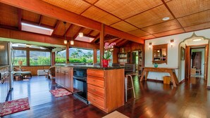 Una cocina amplia con armarios de madera, una isla central y un ventanal con vistas a un paisaje tropical.