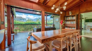 Un comedor de madera con una mesa grande y sillas, una estantería y vistas a un jardín exuberante y montañas.
