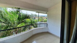 Un balcón con barandilla curva, vistas a zonas verdes y un edificio al fondo.