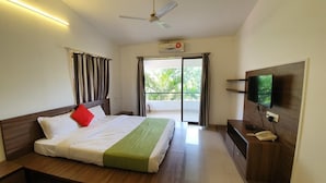 Habitación de hotel con cama, televisión, escritorio con teléfono y balcón con cortinas.