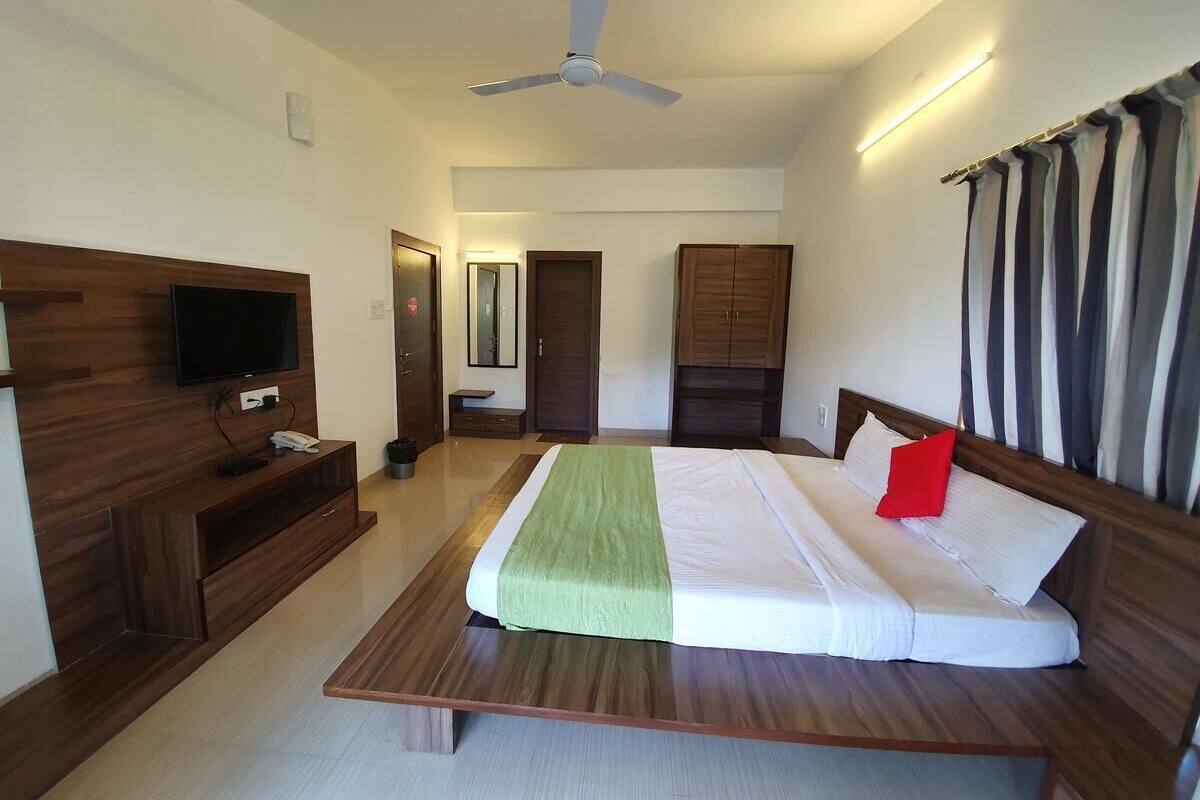 A modern hotel room with a large bed, wooden headboard, a flat-screen TV, a ceiling fan, and a wardrobe.