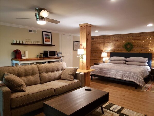 A cozy living room with a sofa, a coffee table, a bed with a headboard, and a wooden accent wall. - Modern Mountain Escape - Private Fireplace & Views (Asheville)