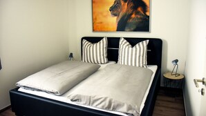 A bed with two pillows, a headboard, and a small bedside table with a lamp. - Barrier-free apartment 14b (Trüben)