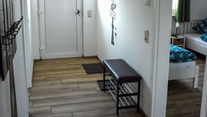 A hallway with a wooden floor, a bench, a white door, and a bed with a green and blue patterned bedspread. - Barrier-free apartment 14b (Trüben)