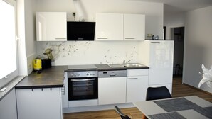 A modern kitchen with white cabinets, a black range hood, a built-in oven, and a sink. - Barrier-free apartment 14b (Trüben)