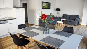 A modern living space with a dining area featuring a white table, black chairs, and a vase with red flowers. - Barrier-free apartment 14b (Trüben)