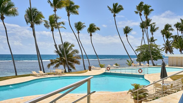 Zona de piscina con palmeras y vista al océano.