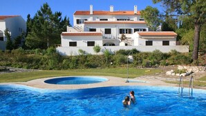 A swimming pool with a clear blue water feature, surrounded by a well-maintained lawn and a large building with a tiled roof in the background.