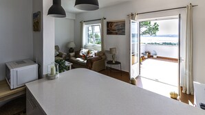 A modern kitchen with a large island, a dining area with a sofa, and a view of the outdoors through a sliding door.