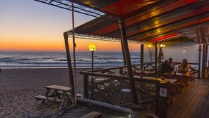 A beachside restaurant with outdoor seating overlooking the ocean at sunset.