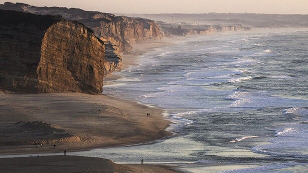 A coastal landscape with a sandy beach and rocky cliffs.