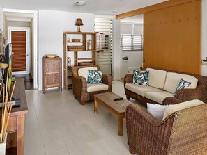 Ein Wohnzimmer mit Korbmöbeln, einem Holzschrank und einem großen Fenster mit Jalousien.