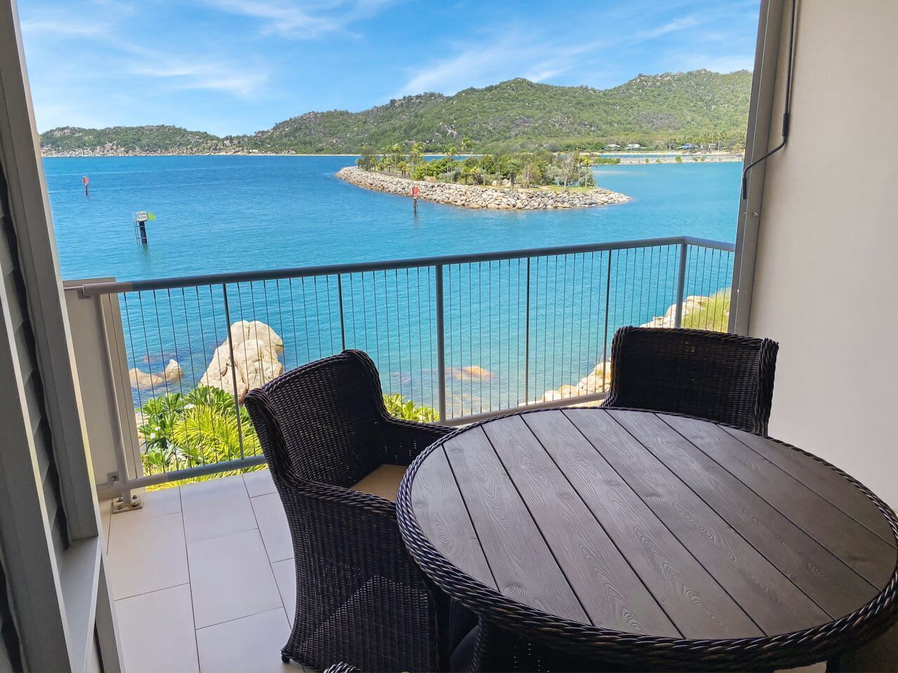 A balcony with wicker furniture and a view of a calm sea and distant hills.