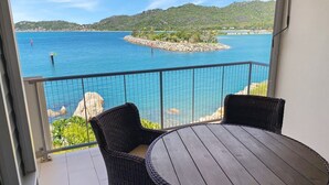 Un balcon agrémenté de meubles en osier, offrant une vue sur une mer calme et des collines lointaines.