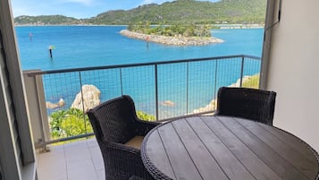 A balcony with wicker furniture and a view of a calm sea and distant hills.