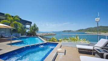 A swimming pool with lounge chairs, a view of the sea, and a modern building.