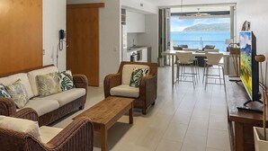 Un salon meublé avec des meubles en osier, une table basse en bois, un canapé et un coin repas offrant une vue sur la mer.