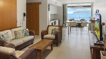A living room with wicker furniture, a wooden coffee table, a sofa, and a dining area with a view of the sea.