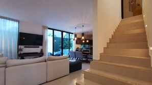 Un salon moderne doté d’un grand canapé, d’un coin repas et d’un escalier menant à l’étage supérieur.