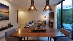 Un salon moderne avec une grande table à manger en bois, deux lampes suspendues, un canapé et un téléviseur.