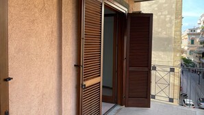 A balcony with wooden shutters, a concrete ceiling, and a view of a city street. - Bluemar Guest House (Castellammare di Stabia)
