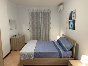 A bedroom with a wooden bed, a nightstand, a dresser, a mirror, a curtain, and wall art. - Bluemar Guest House (Castellammare di Stabia)