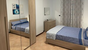 A bedroom with two beds, a mirror, a dresser, and a wall with framed pictures. - Bluemar Guest House (Castellammare di Stabia)