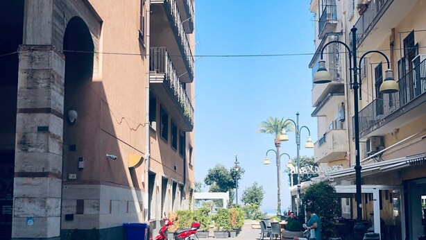 A street with buildings, a parked scooter, and a pedestrian. - Bluemar Guest House (Castellammare di Stabia)