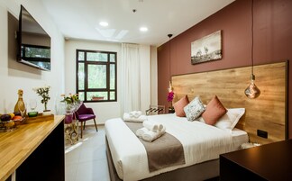 Una habitación de hotel moderna con una cama grande, un escritorio con televisor de pantalla plana, una ventana con cortinas y un cabecero de madera.