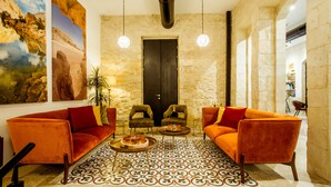 A lobby with two orange sofas, a patterned floor, and a large painting on the wall. - The Negev Hotel (Beersheba)