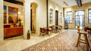 A spacious lobby with a patterned floor, a seating area with tables and chairs, and a large arched doorway. - The Negev Hotel (Beersheba)