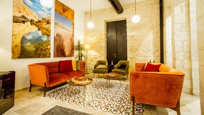 A modern lobby with a red sofa, two armchairs, a patterned rug, and a large painting of a desert landscape. - The Negev Hotel (Beersheba)