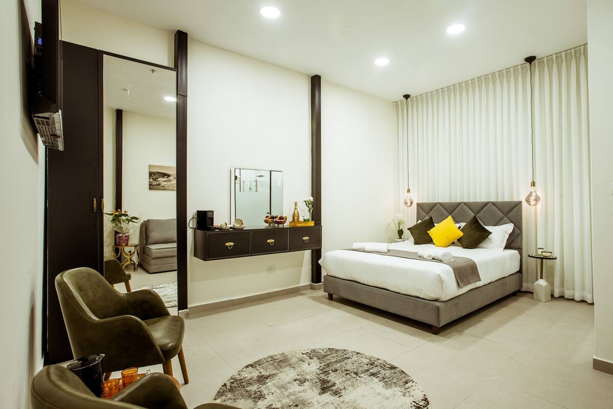 A modern bedroom with a bed, bedside tables, a mirror, a sofa, and a chair.