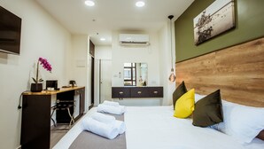 A hotel room with a bed, a desk, a chair, a potted orchid, a mirror, and a wooden headboard. - The Negev Hotel (Beersheba)
