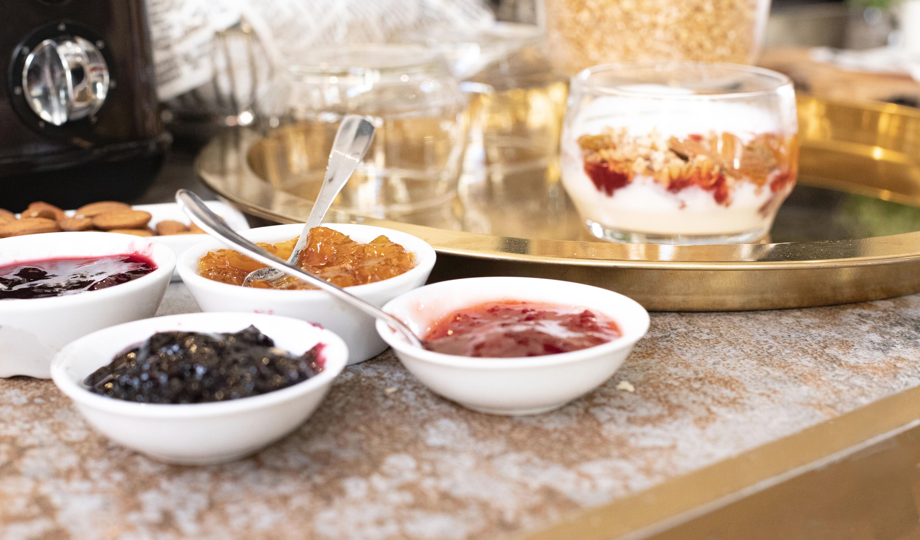 Una variedad de postres en una bandeja, incluyendo recipientes con diferentes tipos de compota y un vaso de parfait de yogur.