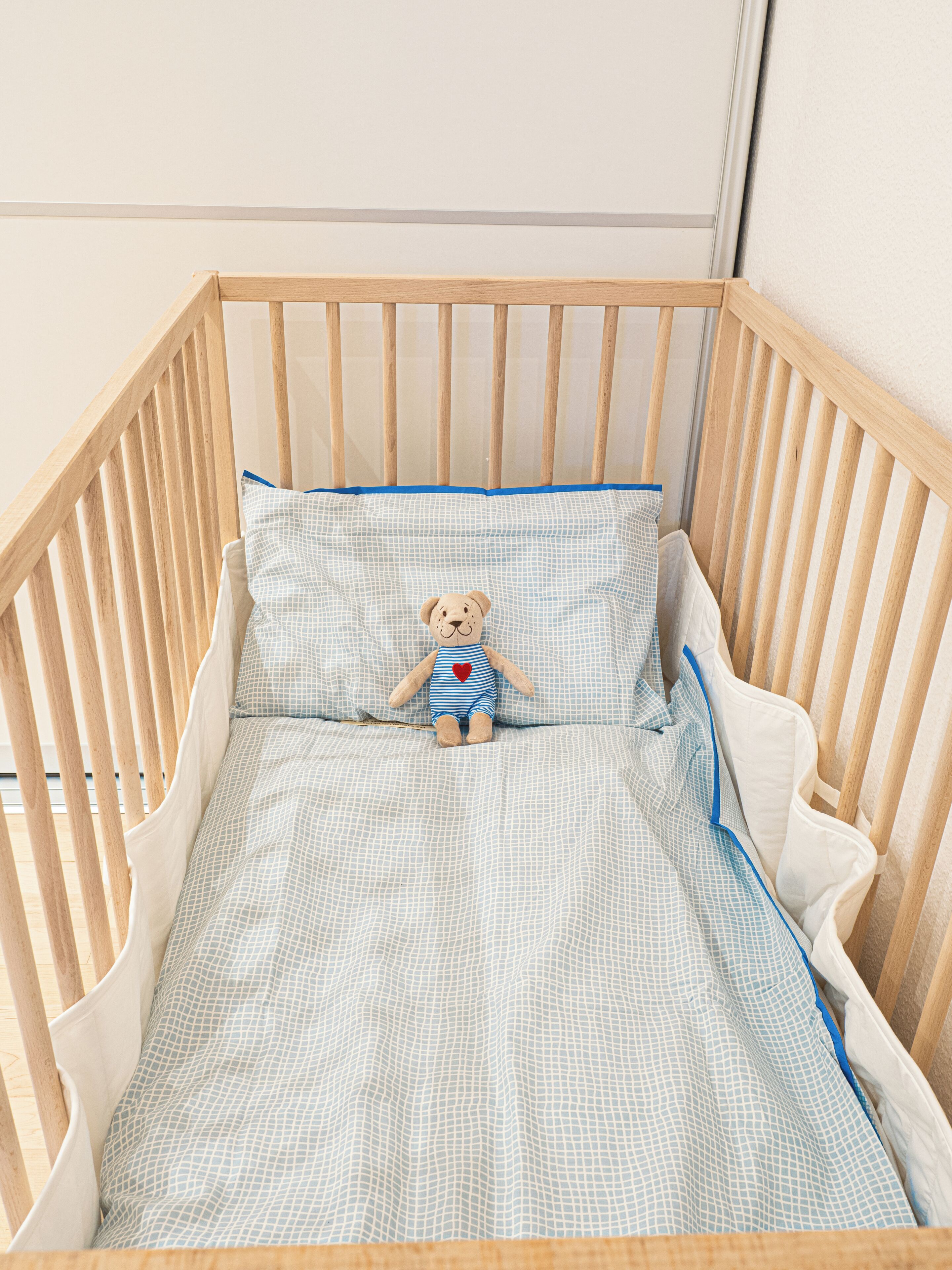 Ein hölzernes Kinderbett mit Matratze und einem Teddybär.