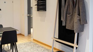 Une pièce avec un plancher en bois, une chaise noire, une table blanche, un tableau noir recouvert de feuilles de papier et un manteau accroché à un porte-manteau en bois.