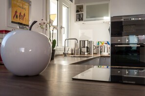 A modern kitchen with a built-in oven, stainless steel appliances, and a large white vase on the counter.
