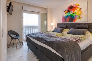 A bedroom with a bed, a chair, a painting, and a balcony.
