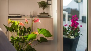 A modern living room with a flat-screen TV mounted on the wall, a small wooden cabinet, and a potted plant with pink flowers.