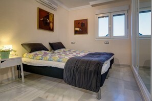 A bedroom with a bed, a bedside table, a lamp, and two wall-mounted paintings.