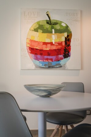 A dining area with a table, chairs, and a colorful apple artwork on the wall.