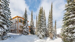 Un paisaje nevado con un edificio de diseño moderno y una pista de esquí al fondo.