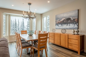 A dining area with a wooden table, chairs, a chandelier, and a painting of horses.